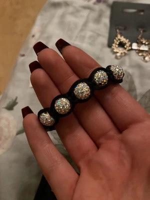 Svart hårsnodd med glittrande pärlor - Säljer en svart hårsnodd dekorerad med fem stora, glittrande pärlor som ger en riktigt lyxig och trendig vibe. Perfekt för att piffa till din frisyr med lite extra bling. Elastiskt band som sitter skönt i håret.