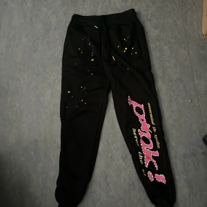 Sp5der byxor - Svarta mjukisbyxor med färgglatt tryck på ena benet och små stjärnmönster. Byxorna har snörning i midjan och muddar vid bensluten. Perfekta för en chill och avslappnad stil.