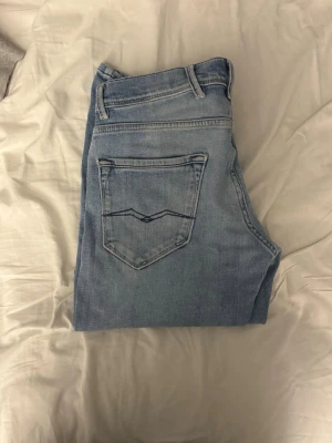 Ljusblå bootcut jeans från Replay - Säljer ett par ljusblå jeans från Replay med klassisk femficksdesign och bootcut passform. Jeansen har snygga detaljer på bakfickorna och är tillverkade i mjukt denimtyg som sitter skönt. Perfekta för en avslappnad och trendig look.