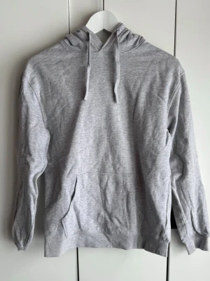 Gråmelerad hoodie. XS. Cubus. - Mjuk, gråmelerad hoodie med huva och dragsnören. Storlek XS. Från Cubus. Borstad insida. Klassisk känguruficka framtill och ribbade muddar vid ärmar och nederkant. Perfekt för en avslappnad look och enkel att matcha med andra plagg. Skrynklig på bilderna, men är i fint skick, inte mycket använd.