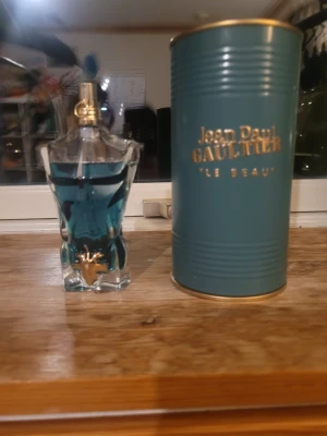 Jean Paul Gaultier Le Beau parfym - Jean Paul Gaultier Le Beau parfym i en unik flaska formad som en manlig torso med blått glas och gulddetaljer. Kommer med originalförpackning i metall med guldfärgad text. En ikonisk doft som sticker ut i badrumshyllan.