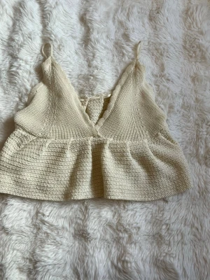 Beige stickad linnetopp med snörning - Supersöt beige stickad linnetopp med smala axelband och v-ringning. Toppen har en lätt volang nedtill och snörning i ryggen för extra detalj. Perfekt för varma dagar och enkel att styla med jeans eller kjol. Det går att spänna på insidan så att den blir tajtare i midjan och axelbanden går också att justera. Måtten finns på bilderna men hör gärna av dig vid frågor🫶