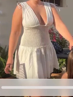Vit kort sommarklänning med volang - Säljer en söt vit kort klänning med volangkant och smock i midjan. Klänningen har djup v-ringning och knytband på axlarna för en justerbar passform. Perfekt inför studenten!!!
