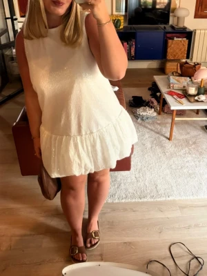 Vit glittrig kortklänning - Supersöt vit kortklänning med glittriga detaljer och volang nedtill. Klänningen är ärmlös och har en rak passform som ger festlig look! Perfekt inför studenten då den är något alldeles extra med massa paljetter men ändå håller sig till ramen då den är vit! Storlek L men liten i storleken! 