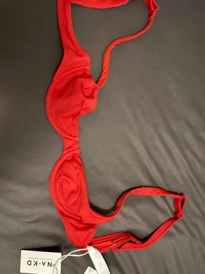 Röd bikiniöverdel från NA-KD - Snygg röd bikiniöverdel från NA-KD med bygel och justerbara axelband. Klassisk och enkel design som ger ett stilrent intryck. Perfekt för strandhäng eller poolparty. Nyskick och oanvänd.