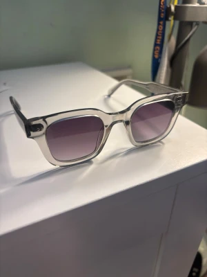 Transparenta solglasögon från Chimi - Säljer ett par stilrena solglasögon från Chimi med transparent båge och rektangulär form. Glasen är mörka med en lätt tonad effekt, modell 04, glasögonen är i bra skick men har repor framtill och bågarna är lite lösare ☺️