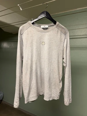 Stone Island långärmad t-shirt - Stone Island långärmad t-shirt i storlek m. Tröjan är grå och tillverkad i 100% bomull, designad medvetet med en sliten, grungig workwear look. Stilren med en subtil logga på bröstkorgen.   Tillverkad i Tunisien.  Originalkvitto från köpet medföljer.  Skick 7/10, burits i många år och fortfarande i bra skick. Ett tydligt bevis på den kvalitet Stone Island är kända för. Några få skador, vänligen se bilder. Svarar gärna på frågor 👍🏻