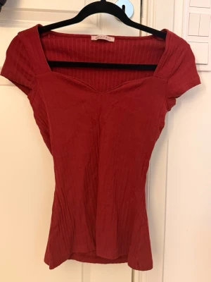 Röd ribbad topp från Anna Field - Trendig röd topp från Anna Field med ribbad struktur och v-ringad hals. Kortärmad och figurnära passform som ger en snygg siluett. Perfekt att styla med jeans eller kjol för en cool look.