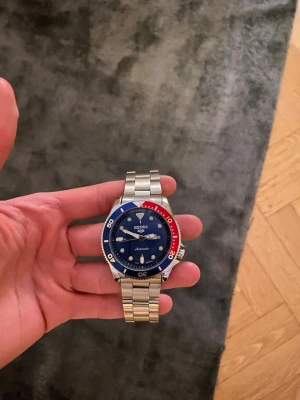 Helt Ny Seiko Mod Sports 5 - Säljer denna helt nya Seiko Mod Sports 5 klockan med marinblå urtavla som visar både datum samt veckodag, och som har en roterande bezel i marinblå och röd färg✅  Klockan har en batteridriven Quartz movement, och den kommer med en klocklåda✅  Vid fler frågor eller funderingar skicka gärna ett pm, Mvh