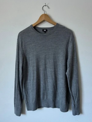 Grå stickad tröja från Uniqlo - Klassisk grå stickad tröja från Uniqlo i mjukt material. Tröjan har rund halsringning, långa ärmar och ribbade muddar vid ärmslut och nederkant. Enkel och stilren design som passar till det mesta. 8D16