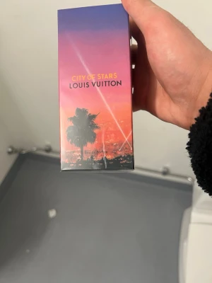 Louis Vuitton City of Stars parfym - Exklusiv parfym från Louis Vuitton, City of Stars, i en snygg förpackning med färgstark solnedgång och palmträd. Förpackningen är rektangulär och rymmer 100 ml Eau de Parfum. Perfekt för dig som gillar lyxiga dofter och stilren design.