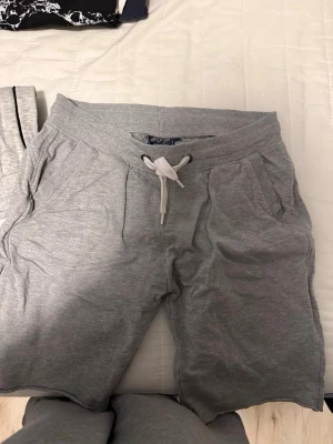 Grå sweatshorts från CJP - Mysiga grå sweatshorts från CJP med dragsko i midjan och två sidofickor. Tillverkade i mjukt sweatshirtmaterial som passar perfekt för chill dagar. Klassisk modell med ribbad midja och avslappnad passform.