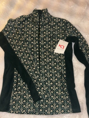 Mönstrad ziptröja från Kari Traa - Snygg ziptröja från Kari Traa med mörkgrönt och vitt mönster, hög krage och hel dragkedja framtill. Tröjan har långa ärmar och är tillverkad i ett mjukt material som passar perfekt för lager-på-lager. Märkeslogga broderad på bröstet. Säljer då den va lite stor på mig🩷 aldrig använd, ny med prislapp. 