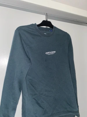 Mörkgrön sweatshirt från Jack & Jones - Mörkgrön sweatshirt från Jack & Jones med vit märke på bröstet med texten Jack & Jones. Varan är i mycket bra skick och knappt använd. Jag säljer den för att jag behöver pengar och vill bli av med gammla kläder. Jag köpte tröjan för 300kr skriv gärna om du är intresserad 