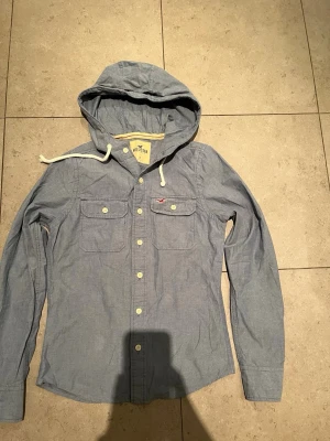 Hollister tröja - Snygg hoodie från Hollister med knappar framtill och två bröstfickor. Tunnare material, perfekt för lager på lager. Klassisk huva med vita snören och diskret Hollister-logga på bröstet. Långärmad och av slappnad passform.