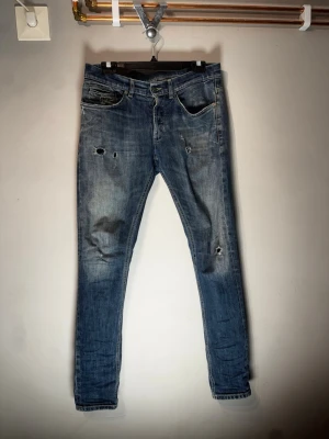 Blå slitna jeans med hål - Säljer ett par blå jeans med slitningar och hål på benen. Jeansen har en klassisk femficksmodell och normal passform. Perfekta för dig som gillar en avslappnad och trendig stil.