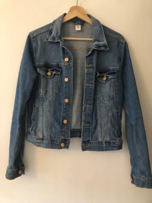 Klassisk blå jeansjacka - Snygg blå jeansjacka med raka sömmar och bröstfickor med knapp. Jackan har metallknappar framtill och vid ärmsluten samt en klassisk krage. Perfekt att slänga över en hoodie eller t-shirt för en avslappnad look.