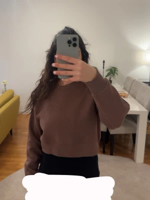 Brun croppad sweatshirt - Säljer en brun croppad sweatshirt med rund hals och långa ärmar. Tröjan har en enkel och clean design utan tryck eller mönster, perfekt att styla med höga jeans eller kjol. Mjuk och skön, passar dig som gillar en avslappnad look. Använd 2 gånger bara. 