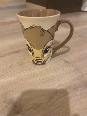 Disney mugg med Bambi och Stampe - Unik mugg i keramik med motiv av Bambi och Stampe från Disney. Muggen är beige och brun med detaljerade illustrationer av karaktärerna på varsin sida. Perfekt för dig som gillar Disney och vill ha något personligt till kaffet eller teet.