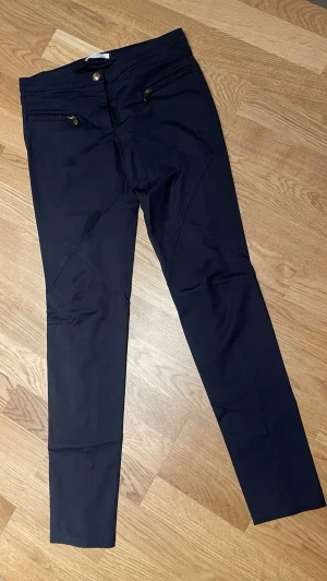 Mörkblåa skinny denim byxor från Versace  stl 36 - Snygga mörkblåa skinny jeans från Versace Collection med guldfärgade dragkedjor på fickorna och coola sömdetaljer. Jeansen har en modern passform och är perfekta för dig som vill ha en stilren och exklusiv look.