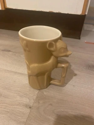 Beige mugg med Bambi - Unik beige mugg i keramik med Bambi som går runt hela muggen och bildar handtaget. Perfekt för dig som gillar djur och vill ha något annorlunda till kaffet eller teet. Muggen har en matt finish och är detaljerad i formen.