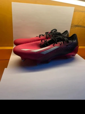 Adidas X Speedflow rosa fotbollsskor - Säljer ett par Adidas X Speedflow fotbollsskor i en snygg rosa och svart färg med vita detaljer. Skorna har klassisk snörning, låg profil och är tillverkade i ett lätt syntetmaterial för maxad speed på planen. Perfekta för dig som vill sticka ut och spela snabbt.