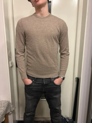 Beige kashmirtröja  - Snygg beige stickad tröja med rund hals och långa ärmar. Tröjan har en slim fit passform och ribbade muddar vid ärmslut och nederkant. Perfekt att matcha med jeans för en clean och stilren look. 100% Kashmir, använd 1-2 gånger. Nyskick. Nypris 1300kr.