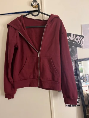 Vinröd hoodie med dragkedja XS - Säljer en vinröd hoodie från 157 i storlek XS. Hoodien har dragkedja framtill, två stora fickor och en klassisk huva. Tillverkad i mjukt bomullsliknande material och har ribbade muddar vid ärmar och nederkant. Perfekt för chill dagar eller när du vill vara extra bekväm.