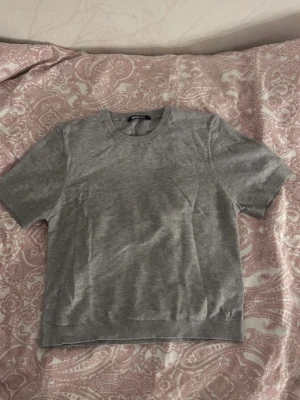 Grå basic t-shirt från Gina Tricot - En enkel och stilren grå t-shirt från Gina Tricot. T-shirten har rund halsringning och korta ärmar. Perfekt till jeans eller kjol för en clean look. Materialet känns mjukt och bekvämt, troligtvis i bomull.