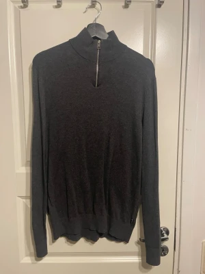 Mörkgrå halvzip tröja - Mörkgrå långärmad tröja med halvzip och hög krage. Tröjan har ribbade muddar vid ärmslut och nederkant. Perfekt för lager-på-lager och enkel att matcha med olika outfits.