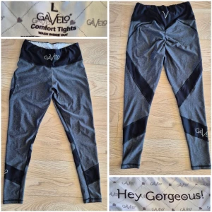Gavelo grå leggings med svarta detaljer - Gråa träningstights från Gavelo med svarta paneler längs benen och hög midja. Tightsen har logga på midjan och nedre benet, samt är tillverkade i ett stretchigt och bekvämt material. Scrunch butt. Använda ett fåtal ggr och således i fint skick.