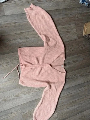 Ljusrosa stickad tröja med snörning - Supersöt ljusrosa stickad tröja med v-ringning och snörning framtill som ger en snygg rynkeffekt. Tröjan har långa ärmar och är ribbstickad för extra mysig känsla. Perfekt att styla med jeans eller kjol för en trendig look.