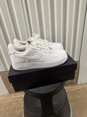 Nike Air Force 1 '07 Flyease Vita Sneakers strl 42 - Klassiska Nike Air Force 1 sneakers i helvitt läder med perforerad tå, vit sula och ikonisk Swoosh på sidan. Skorna har lågt skaft och vita skosnören. Perfekta för en clean och stilren look.
