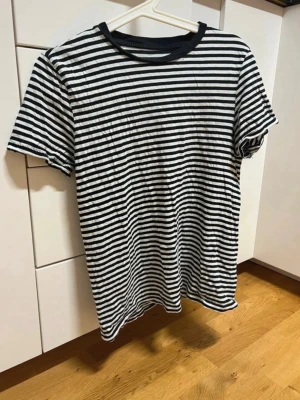 Svartvit randig t-shirt - En klassisk svartvit randig t-shirt med rund hals och korta ärmar. Perfekt för en avslappnad stil och enkel att matcha med jeans eller shorts. Tillverkad i mjukt bomullsmaterial för skön komfort.