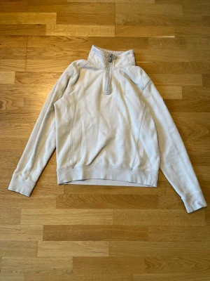 Beige halvzip från Pelle P - Snygg beige tröja från Pelle P med halv dragkedja och hög krage. Tröjan har långa ärmar och en stilren logga på ärmen. Perfekt för lager-på-lager och chill vardagsstil.