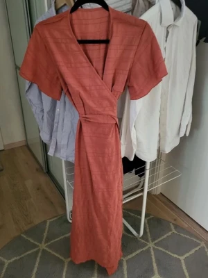 Klänning även i röd färg - Storlek XS. Aldrig använd, endast testad. Inga fläckar eller skador.  Fin omlottmodell med knyt i midjan och korta ärmar. Sitter jättefint på.  Har även exakt samma klänning i röd som jag också säljer.