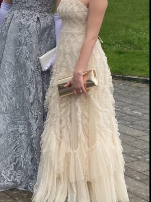 Needle and Thread Balklänning - Säljer min fina fina balklänning från N&T ”Rosella Ruffle Strapless Gown” som först är köpt här på plick i storlek 32. Men en korsett rygg syddes till så den passar nu flera olika storlekar i bysten. Jag har storlek 36. Färgen är champagne, midja: 60cm, höft: 87cm, byst: justerbar. Jag är 160 och hade ett par låga klackar på mig. Den är kemtvättad, så den är som ny! Det är bara att skriva om man har frågor eller vill ha fler bilder🥰(säljer även clutchen i annat inlägg om man vill köpa till)