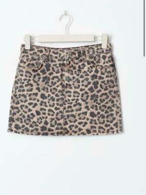 Leopardmönstrad jeanskjol - Cool kort jeanskjol från Gina Tricot med leopardmönster i beige och svart. Kjolen har klassisk femficksdesign, bälteshällor och knappstängning framtill. Perfekt för dig som vill sticka ut med en trendig look.