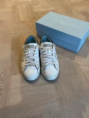 Vita Philippe Model sneakers - Snygga vita sneakers från Philippe Model med klassisk låg siluett. Skorna har vita skosnören, diskreta grå detaljer och svart hälparti. Tillverkade i läder med en stilren design och bekväm passform. Perfekta för en clean och stilig look priset kan diskuteras 😁