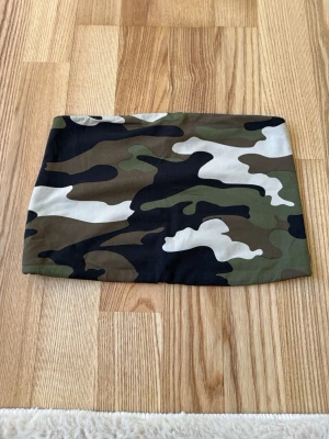Camouflage tubtopp - Snygg tubtopp med camouflage-mönster i grönt, svart, brunt och vitt. Perfekt att styla med jeans eller kjol för en cool och avslappnad look. Gjord i mjuk bomull med stretch för skön passform.