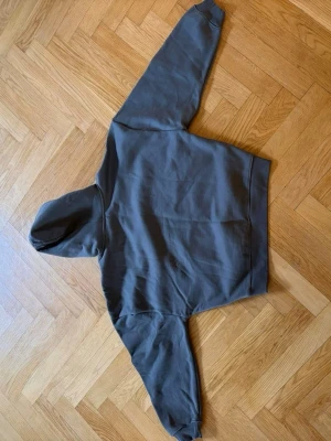 Mörkgrå hoodie med huva - En stilren mörkgrå hoodie med huva och ribbade muddar. Hoodien har en klassisk passform och är tillverkad i mjukt material, perfekt för en avslappnad look. Inga synliga loggor eller tryck, vilket gör den enkel att matcha med andra plagg.