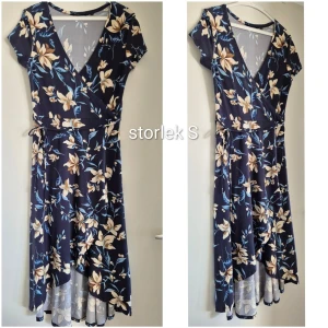 Blommig omlottklänning marinblå - Underbart skön, mjuk, stretchig marinblå omlottklänning med blommigt mönster i beige och ljusgult. Klänningen har v-ringning, korta ärmar och knyt i midjan. Nederdelen är asymmetrisk med volangdetalj och spetskant. Perfekt för sommarens alla tillfällen. 