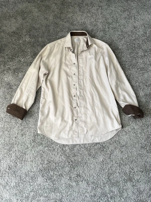 Beige stenström skjorta - Stilren beige skjorta från stenström med bruna kontrastdetaljer på insidan av kragen och manschetterna. Skjortan har klassisk krage, knappar framtill och långa ärmar. Perfekt för dig som vill ha en snygg och tidlös look. Str 41. Nyskick. Pris 399.