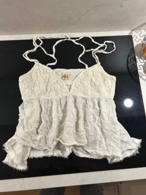 Vit spetslinnetopp från Hollister med spets - Supersöt vit linnetopp från Hollister med spets upptill och volangig nederdel. Tunna axelband och v-ringad halsringning ger en romantisk vibe. Perfekt för varma dagar och somriga outfits.