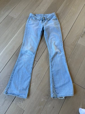Ljusblå bootcut jeans från Cross - Ljusblå bootcut jeans från Cross Jeanswear Company i 100% bomull. Klassisk femficksmodell med låg midja och utsvängda ben. Perfekta för dig som gillar retrostil och vill ha ett par bekväma jeans med snygg passform.