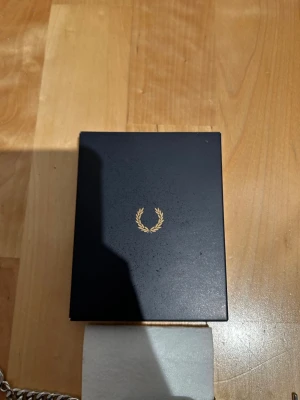 Silverarmband från Fred Perry - Snyggt silverfärgat armband från Fred Perry med kedjelänk och graverad logotyp på plattan. Kommer i original ask med den klassiska Fred Perry-kransen. Perfekt accessoar för att lyfta din stil.