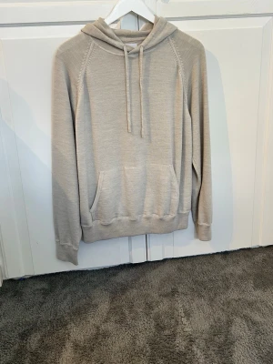 Beige hoodie med ficka framtill - Snygg beige hoodie med huva och dragsko, samt en stor känguruficka framtill. Tillverkad i mjukt stickat material och har långa ärmar med ribbade muddar. Perfekt för en avslappnad och stilren look.100% merinoull. Köpt i Italien. Inget slitage. Ställ gärna frågor 👋