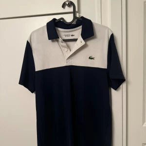Lacoste Sport blåvit pikétröja S - Snygg pikétröja från Lacoste Sport, Stor Lacoste-logga på ryggen och krokodilmärke på bröstet. Perfekt för en sportig och stilren look.