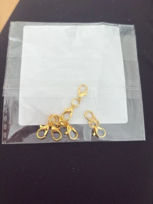 Guldfärgade smyckeslås karbinhakar - Säljer ett set med små guldfärgade karbinhakar för smyckestillverkning. Perfekta att använda som lås till armband, halsband eller andra DIY-projekt. Tillverkade i metall med blank finish och enkel öppningsmekanism.