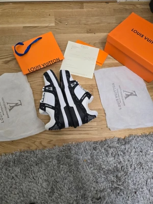 Louis Vuitton svartvita sneakers - Säljer ett par snygga Louis Vuitton sneakers i svart och vitt. Skorna har klassisk LV-logga på plösen och sidan, samt monogramdetaljer i svart på ovandelen. Tillverkade i läder med vita snören och robust sula. Perfekta för dig som vill sticka ut med exklusiv streetstyle.